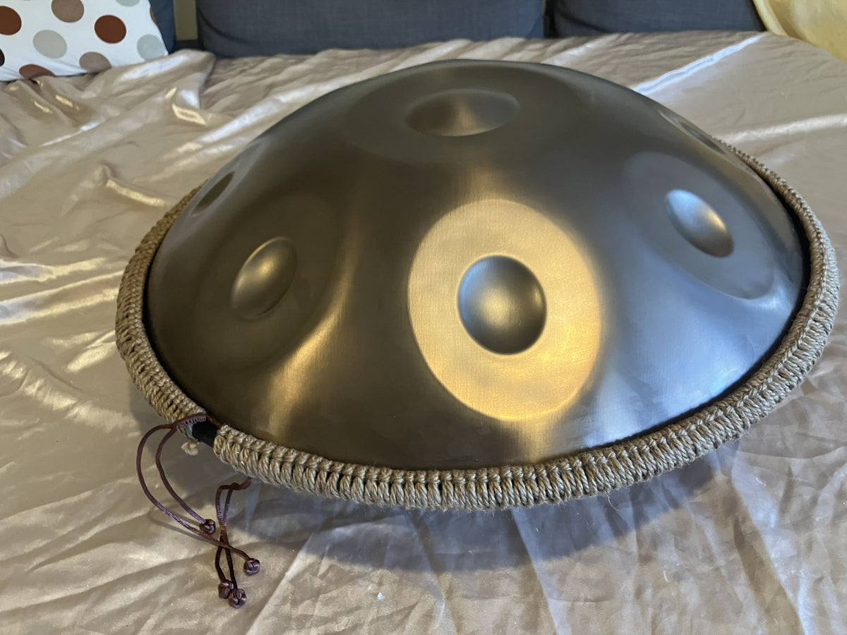 Metallic handpan with braided rim resting on white bedding