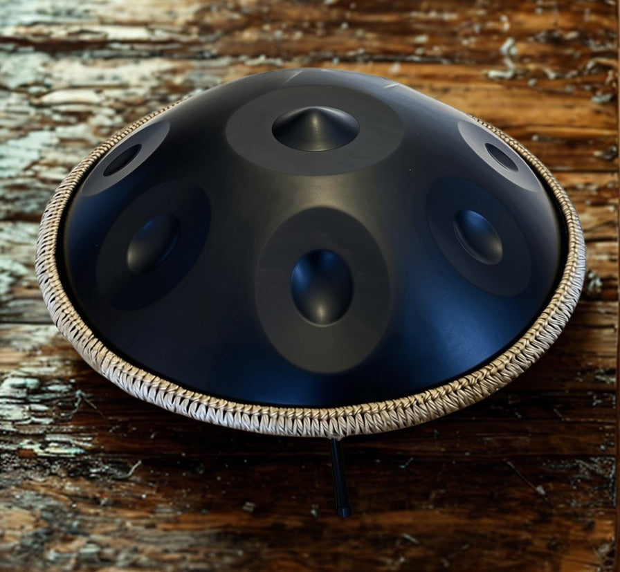 Black handpan with braided rim on a rustic wooden surface