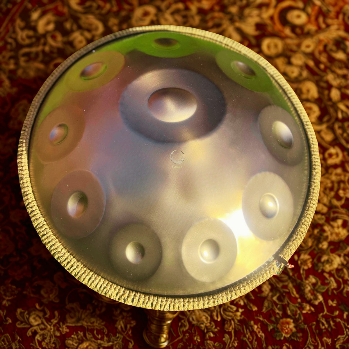 Gold-toned handpan viewed from above on a patterned rug
