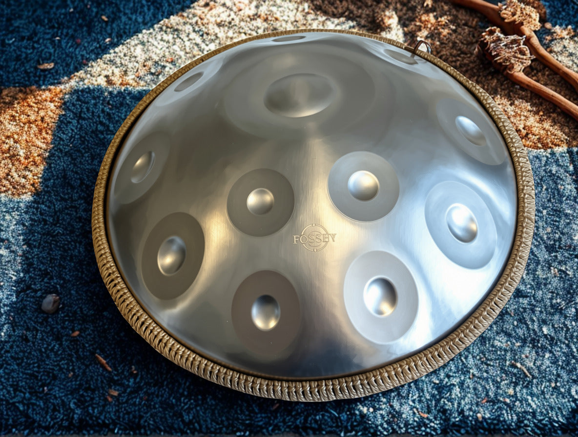 Silver-toned Fossey handpan with braided rim on a blue rug
