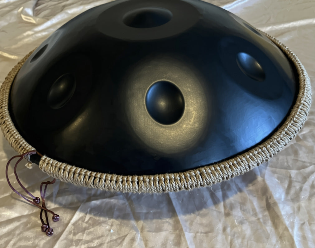 Close-up of a black handpan with braided rim on pale fabric