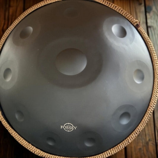 Top view of a black Fossey handpan with gold braided rim on wooden boards. Black Star Fossey Handpan, 10-Note D Kurd, Stainless Steel, 22"