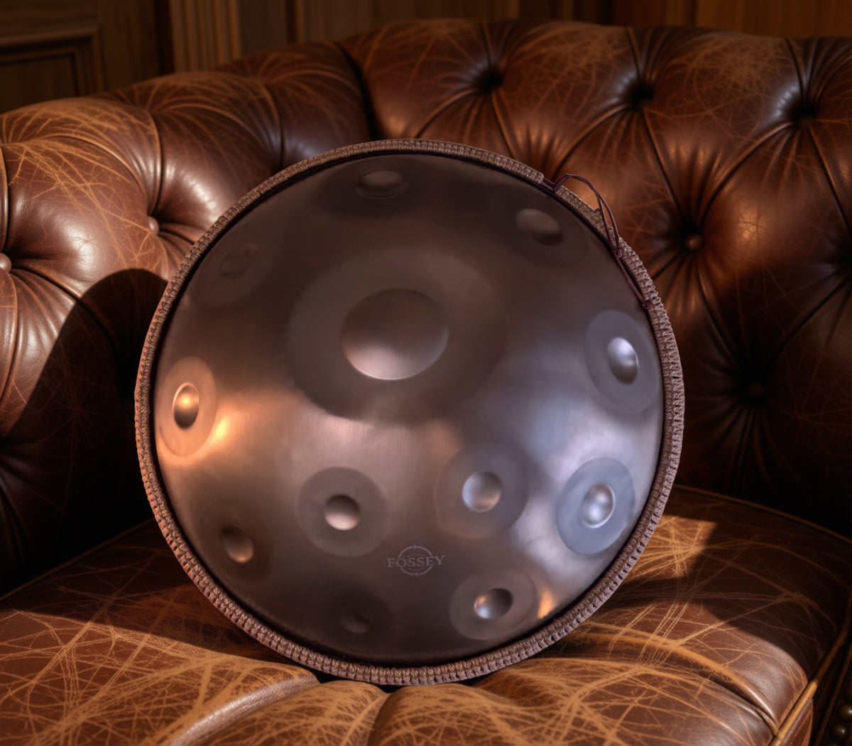 Fossey handpan displayed upright on a brown leather sofa. Gold Standard Fossey Handpan, 12-Note D Kurd, Stainless Steel, 