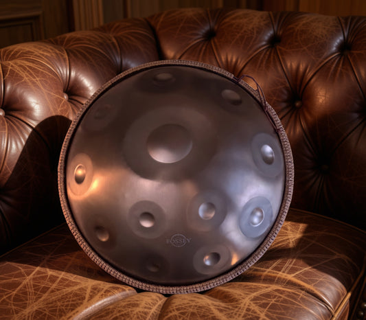 Fossey handpan displayed upright on a brown leather sofa. Gold Standard Fossey Handpan, 12-Note D Kurd, Stainless Steel, 