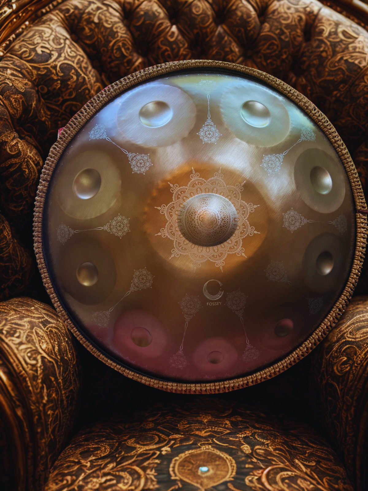 Gold Yantra handpan with engraved mandala design on a patterned armchair.