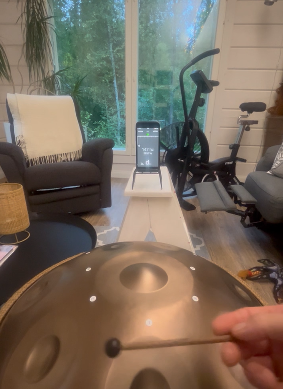 Handpan being struck with a mallet beside a phone displaying a tuner