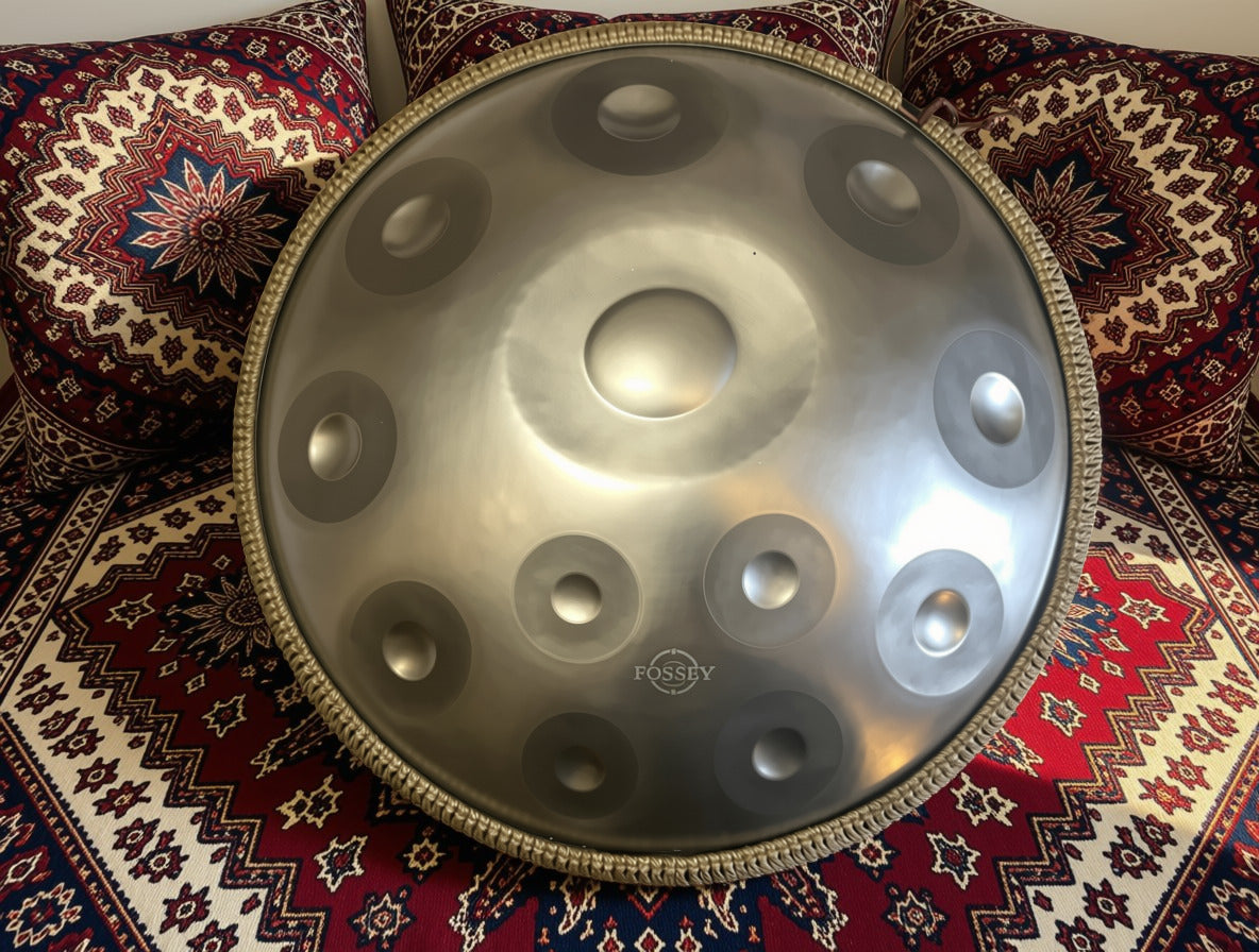 Metallic Fossey handpan propped upright on red patterned cushions. Silver Shine Fossey Handpan - 12-Note, 440hz, D Kurd, Stainless Steel