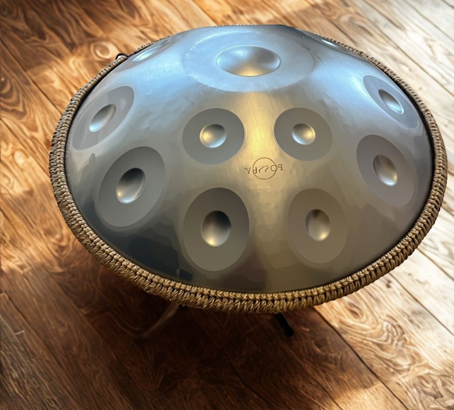 Metallic handpan with braided rim on sunlit wooden floorboards. Silver Shine Fossey Handpan - 12-Note, 432hz, D Kurd, Stainless Steel