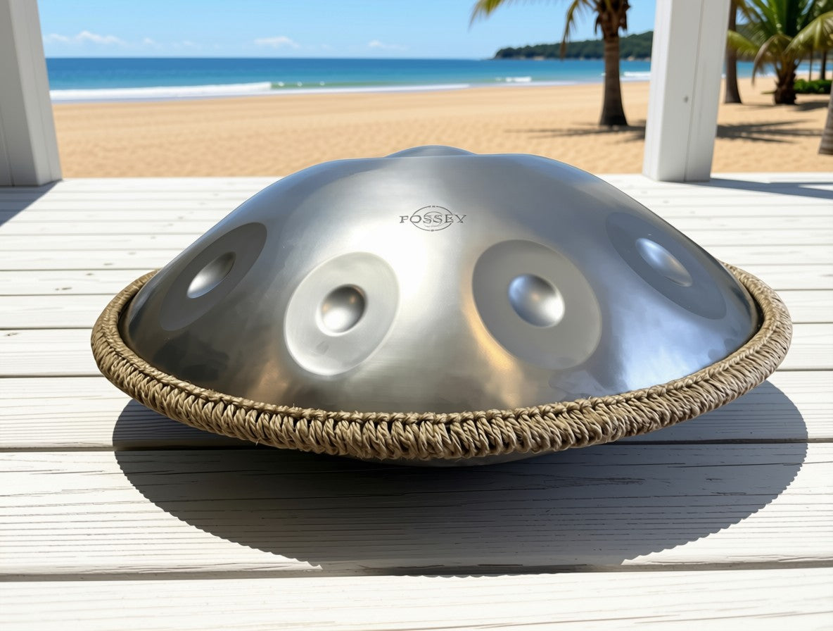 Silver-toned Fossey handpan on a white wooden deck overlooking a sandy beach. Silver Shine Handpan - 9-Note, 440hz, D Kurd, Stainless Steel