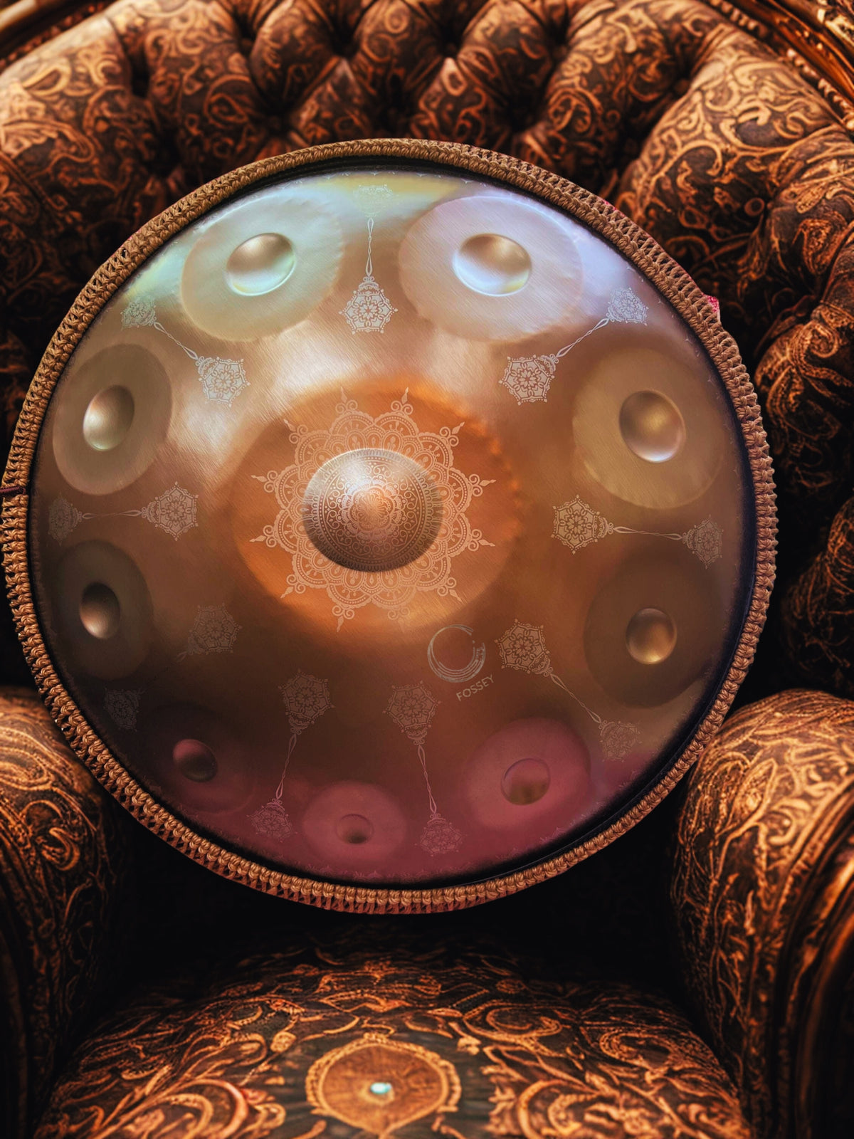 Gold Yantra handpan with engraved mandala design on a patterned armchair