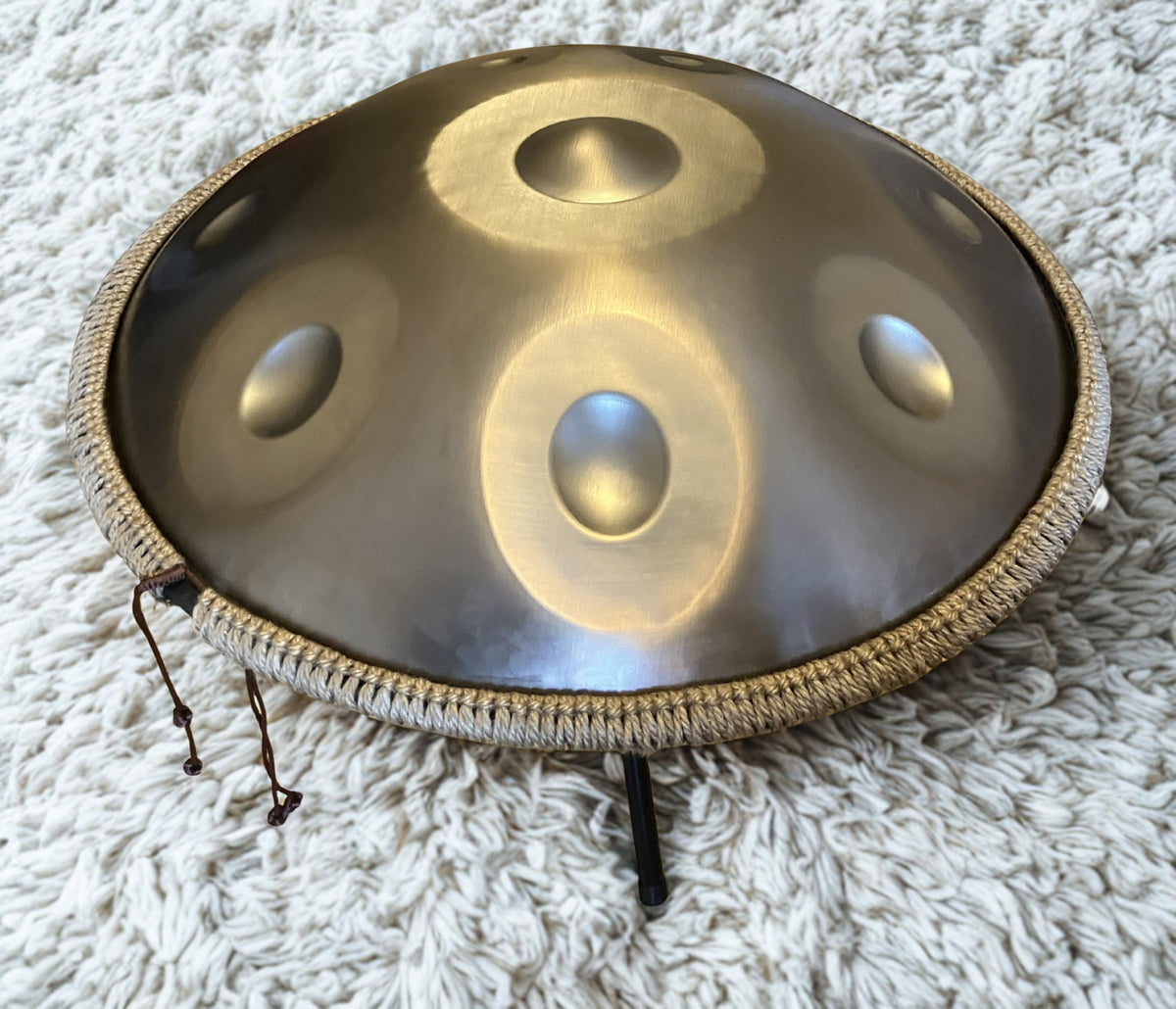 Metallic handpan with braided rim on a small stand over a white rug