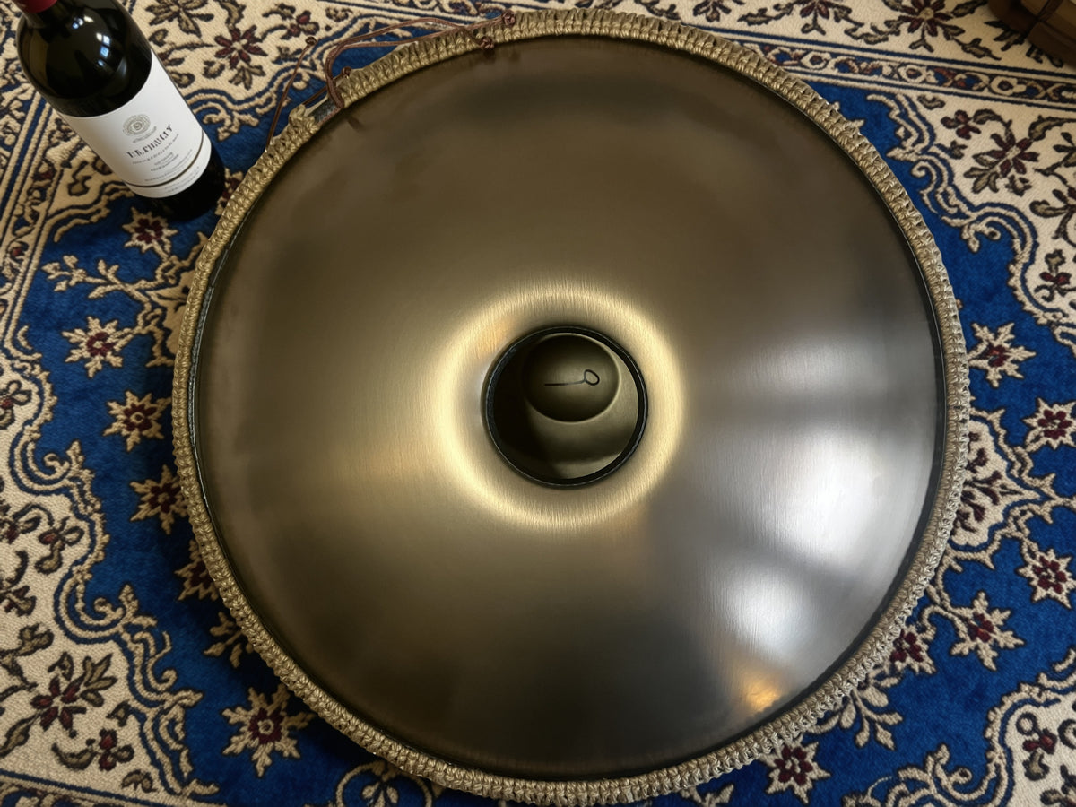 Underside of a metallic handpan on a blue patterned rug beside a wine bottle