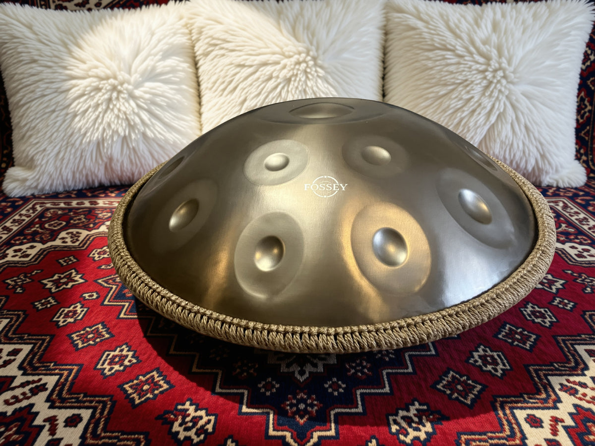 Fossey handpan with braided rim on a red patterned sofa beside white cushions