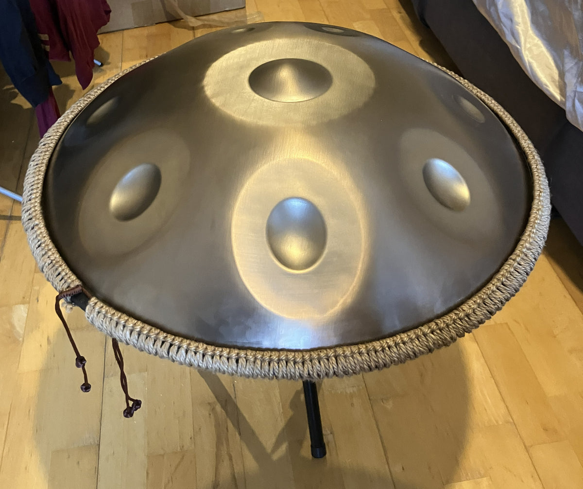 Underside of a metallic handpan with a central sound hole and two tone fields on a stand