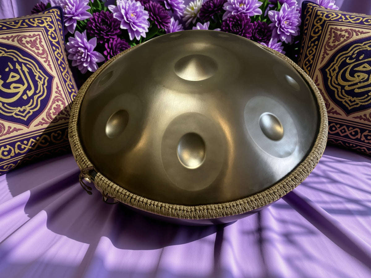 Underside of a metallic handpan with two tone fields on purple fabric beside flowers