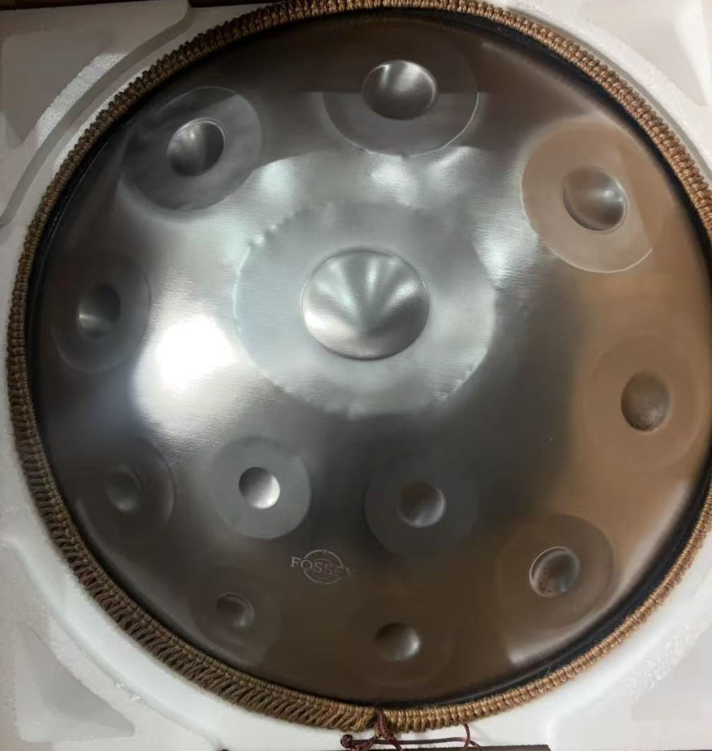 Top view of a silver-toned Fossey handpan with braided rim in protective packaging